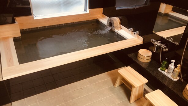 A modern bathroom with a wooden bathtub, a large mirror, and a wooden bench. - Nara Ryokan (Nara)