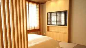 A bedroom with a bed, a TV mounted on the wall, and a window with wooden blinds. - Nara Ryokan (Nara)