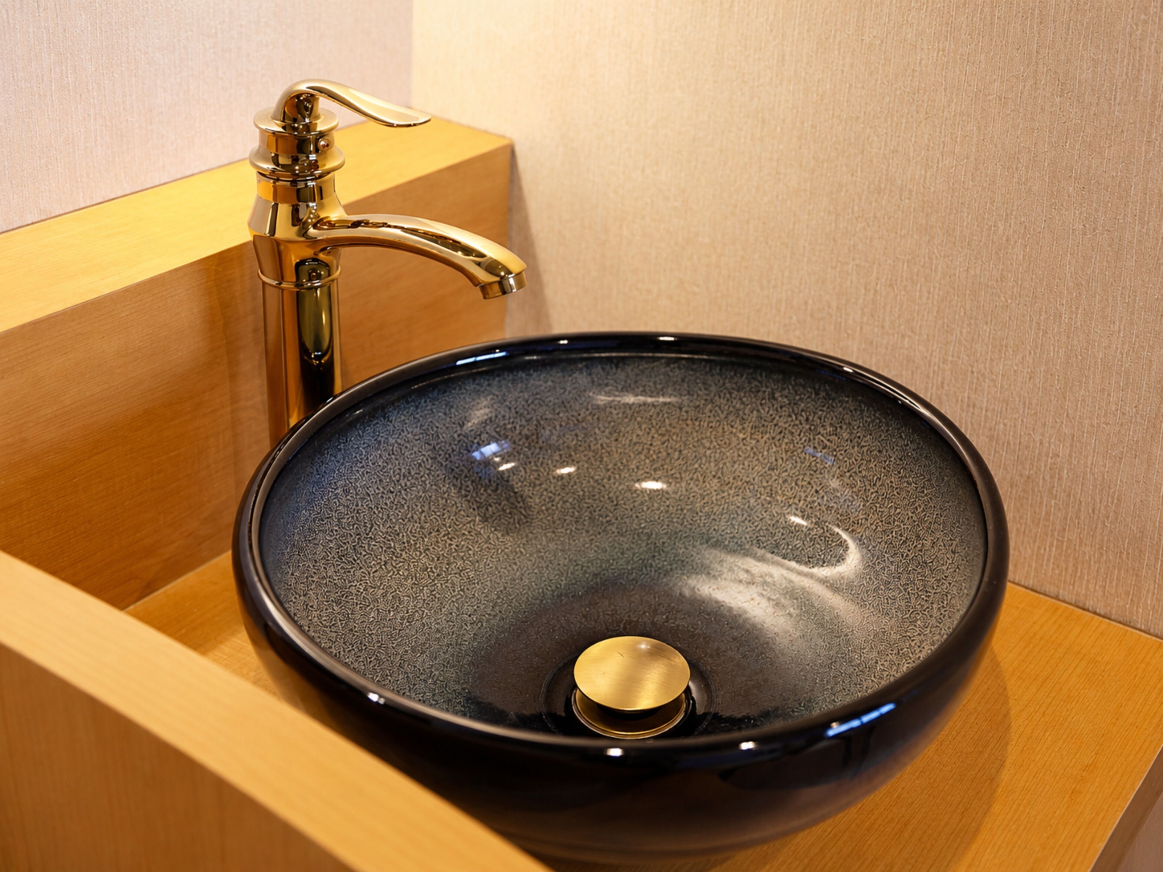 A black ceramic sink with a gold faucet in a wooden cabinet.