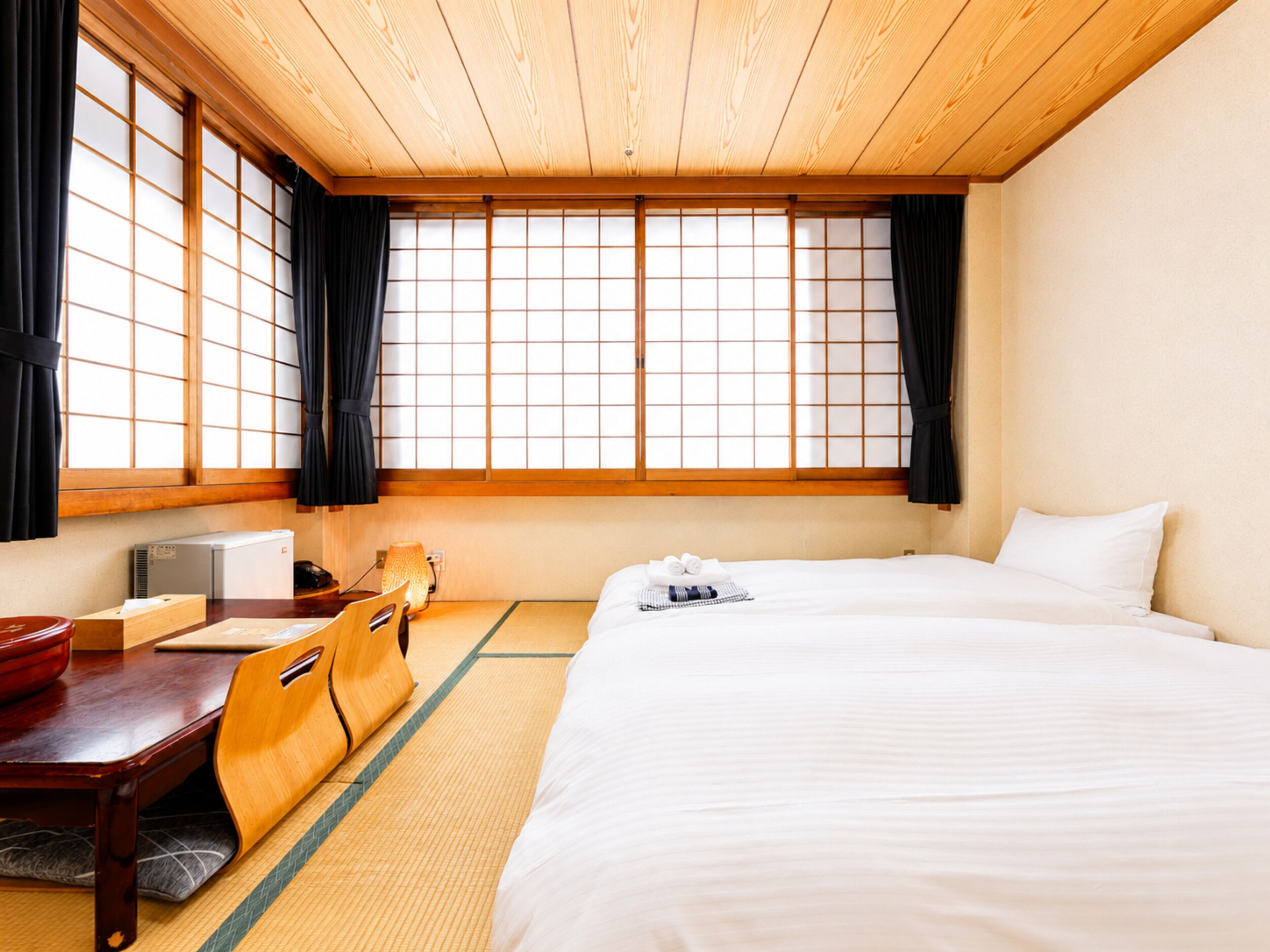 A hotel room with tatami flooring, a bed, a desk with a chair, a heater, and a window with a view.