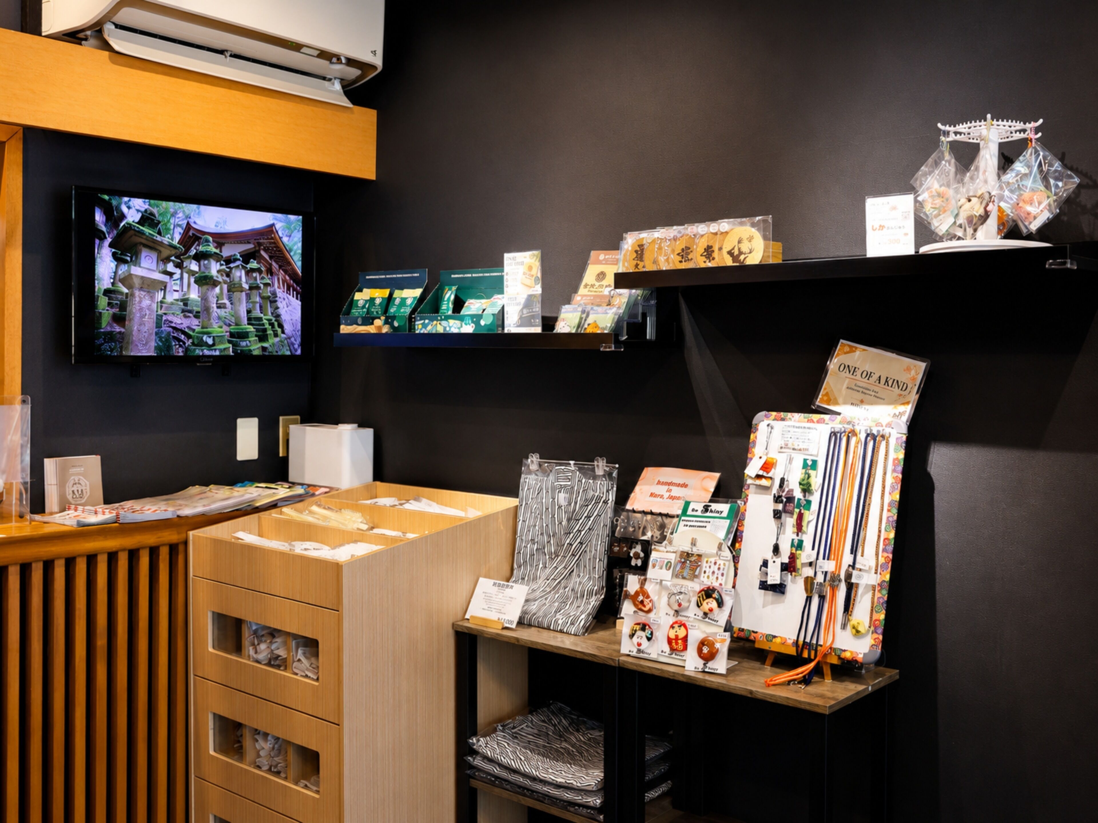 A reception area with a TV displaying a scenic view, wooden furniture, and various items on shelves including boxes and decorative objects.