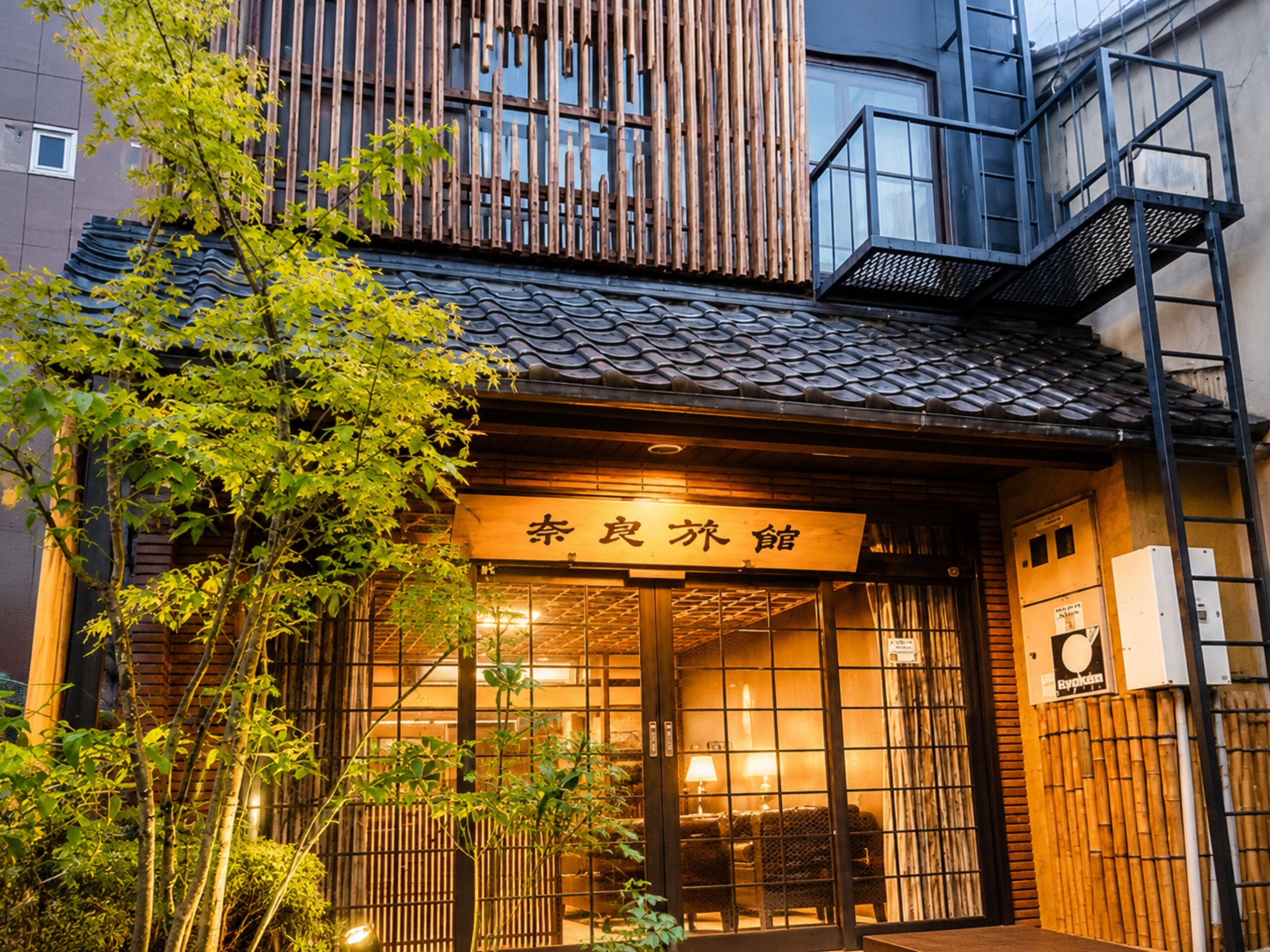 A traditional Japanese building with a wooden exterior, a signboard with Japanese characters, and a small outdoor seating area.