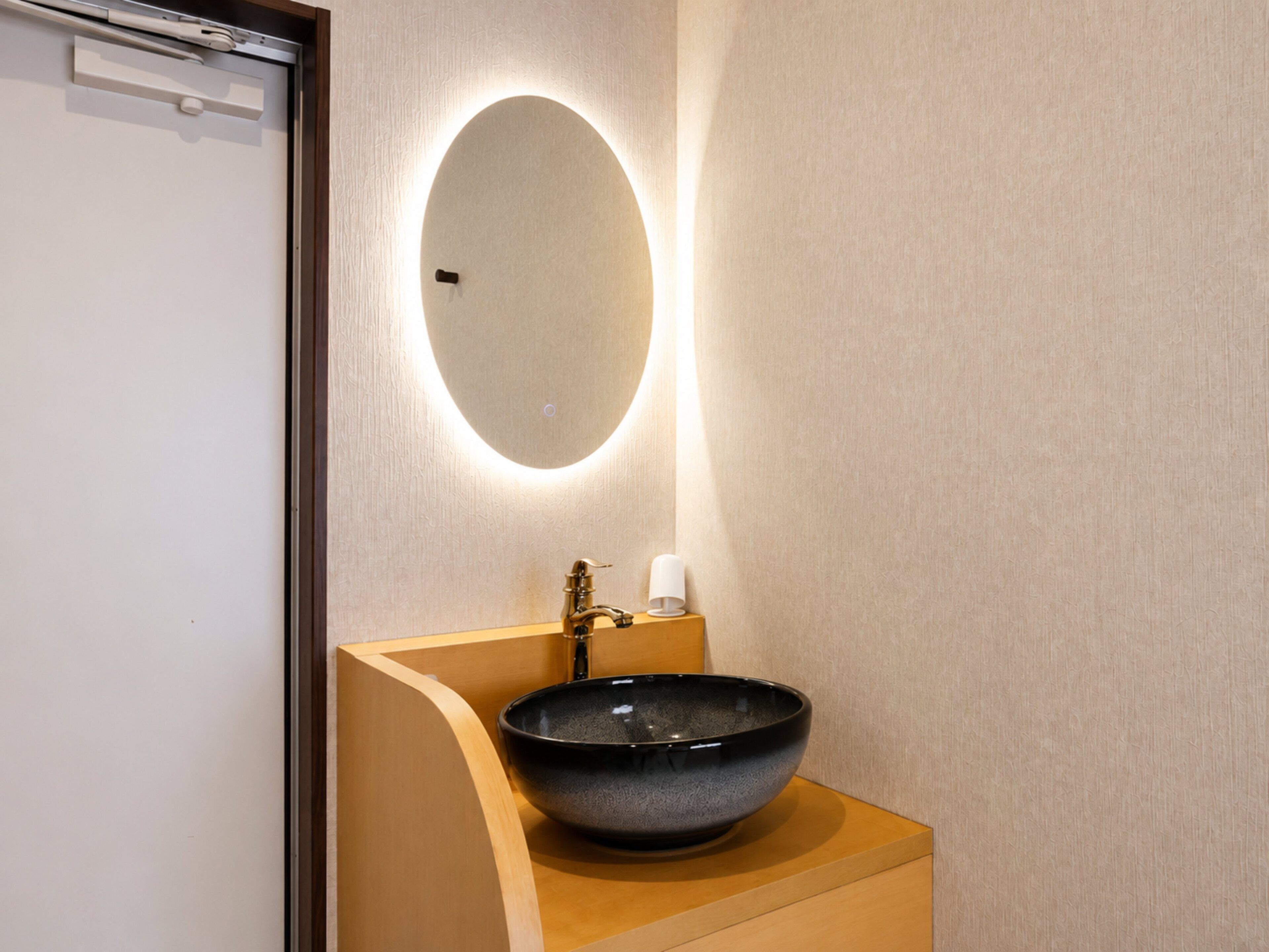 A bathroom with a round mirror, a black vessel sink, and a white cup.