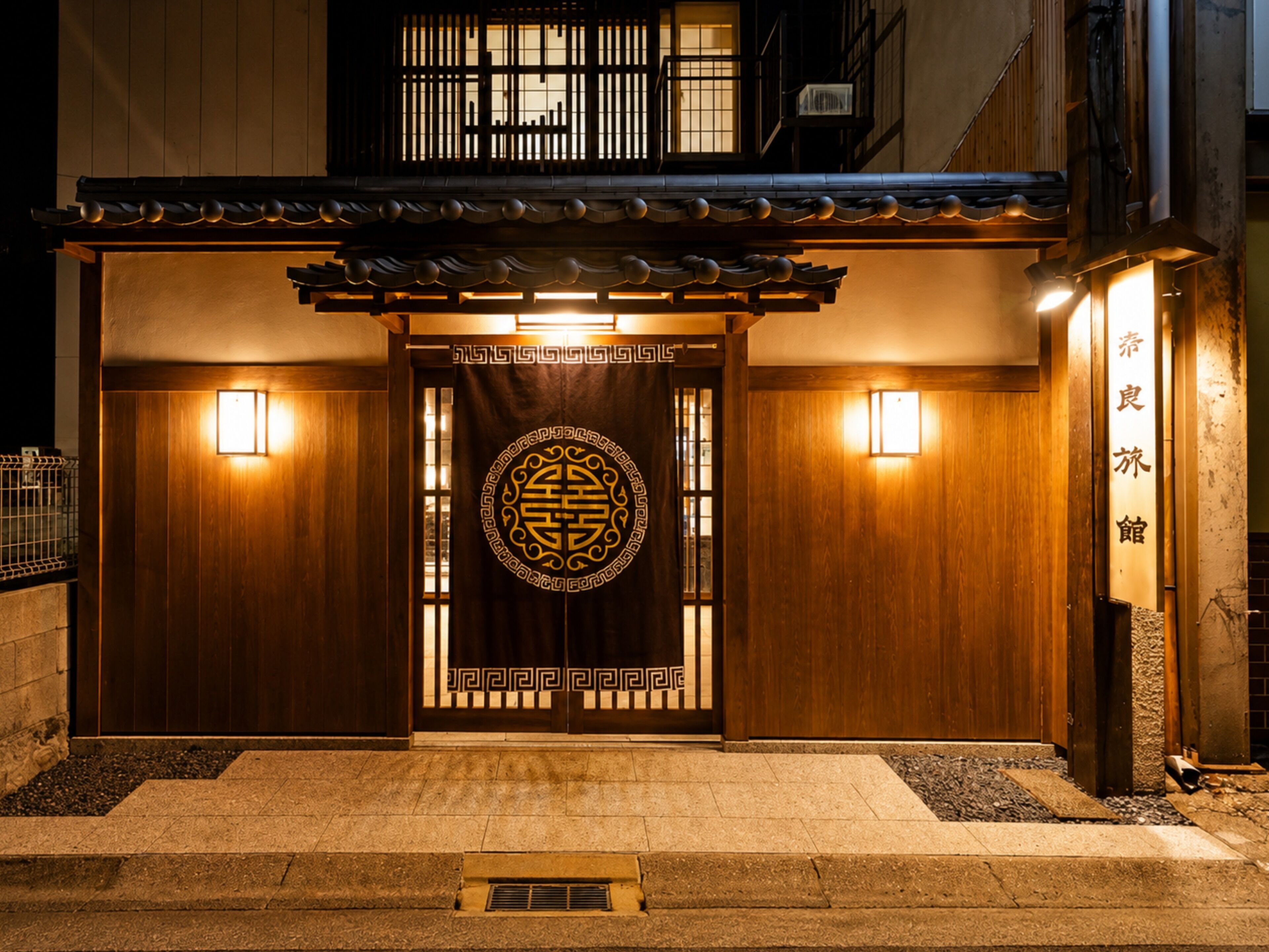 A traditional Japanese building with a wooden facade, a decorative entrance gate, and two wall-mounted lights.