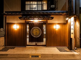 Un edificio japonés tradicional con fachada de madera, una puerta de entrada decorativa y dos luces fijadas a la pared.