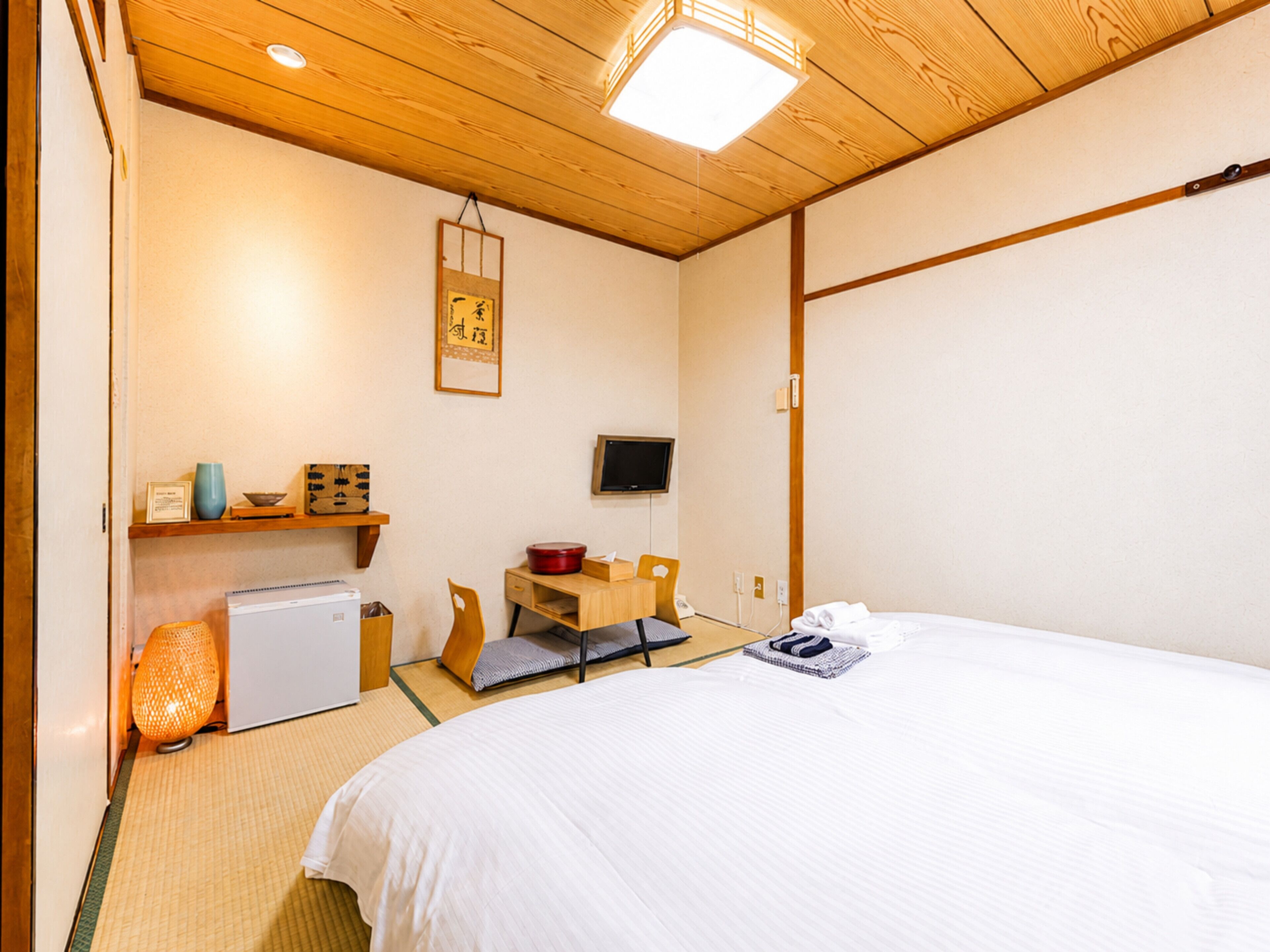 Um quarto com uma cama, uma escrivaninha, uma televisão e uma prateleira com objetos.