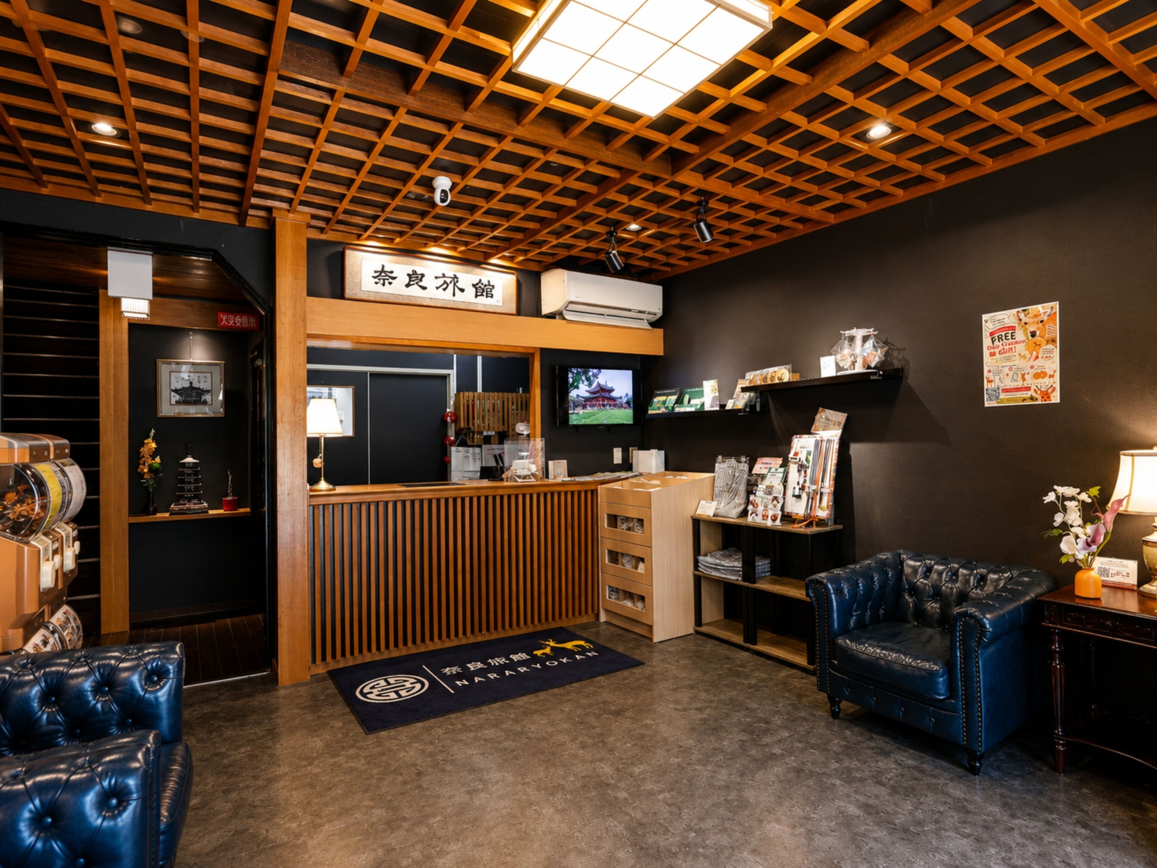 Una zona de recepción con un mostrador de madera, una pared negra con un televisor montado y un sofá de cuero azul.