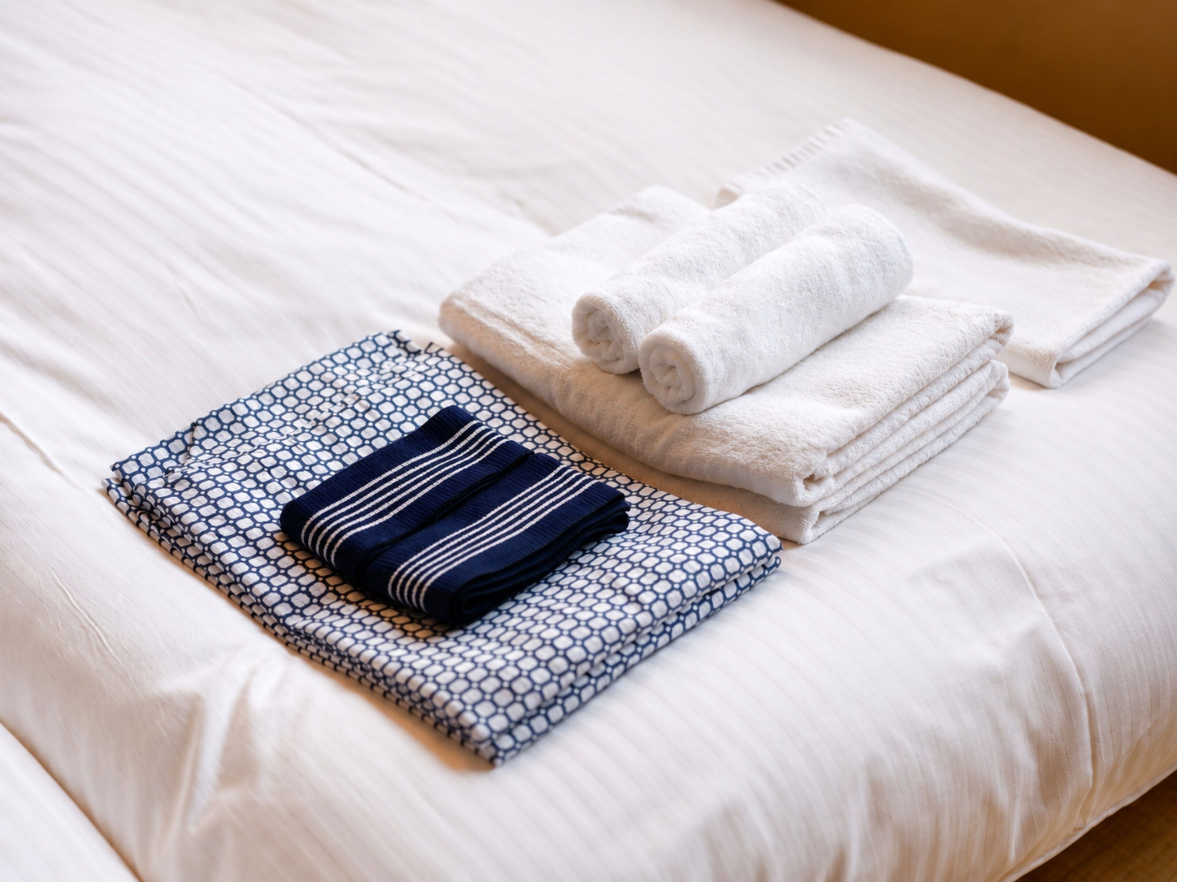 A neatly made bed with white linens and a folded blue and white patterned towel.