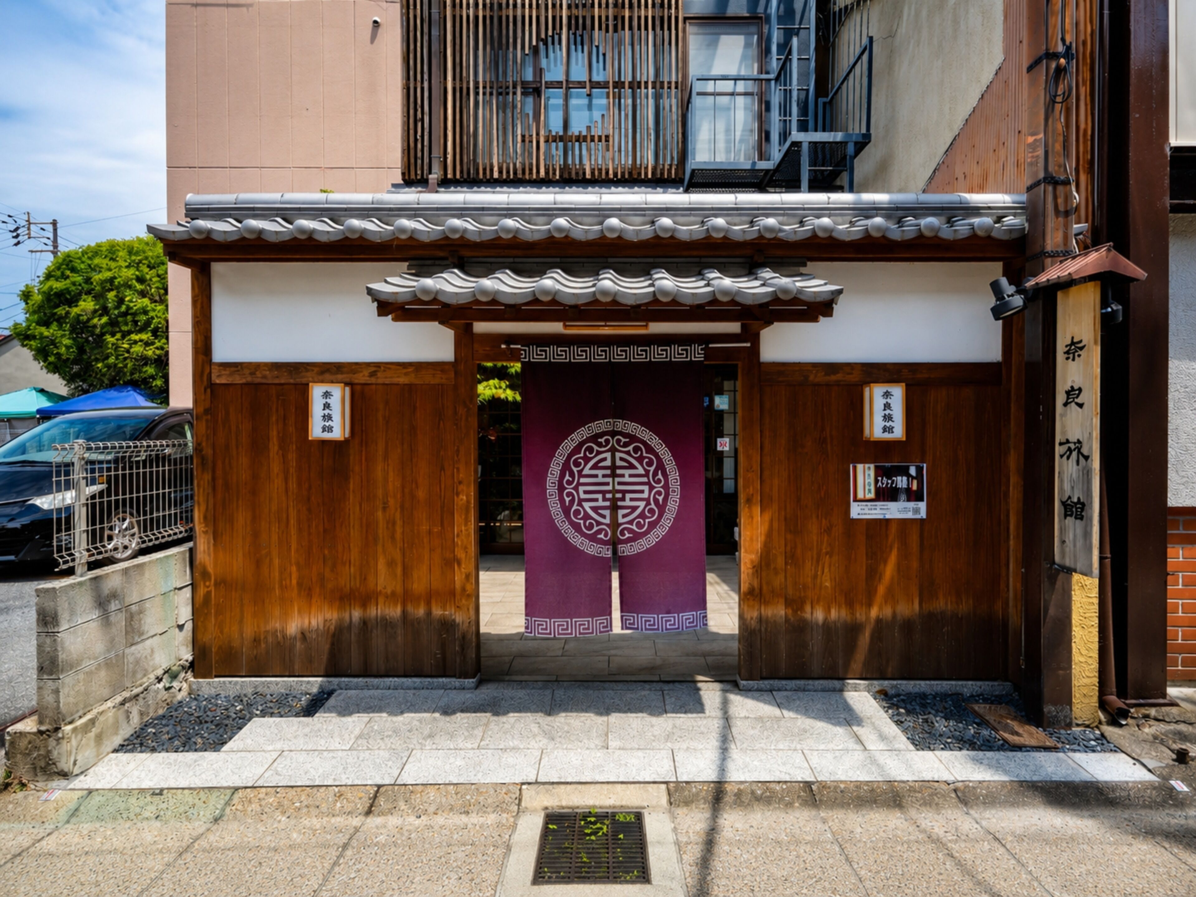 A traditional Japanese building entrance with a wooden gate, a decorative emblem, and a signboard.