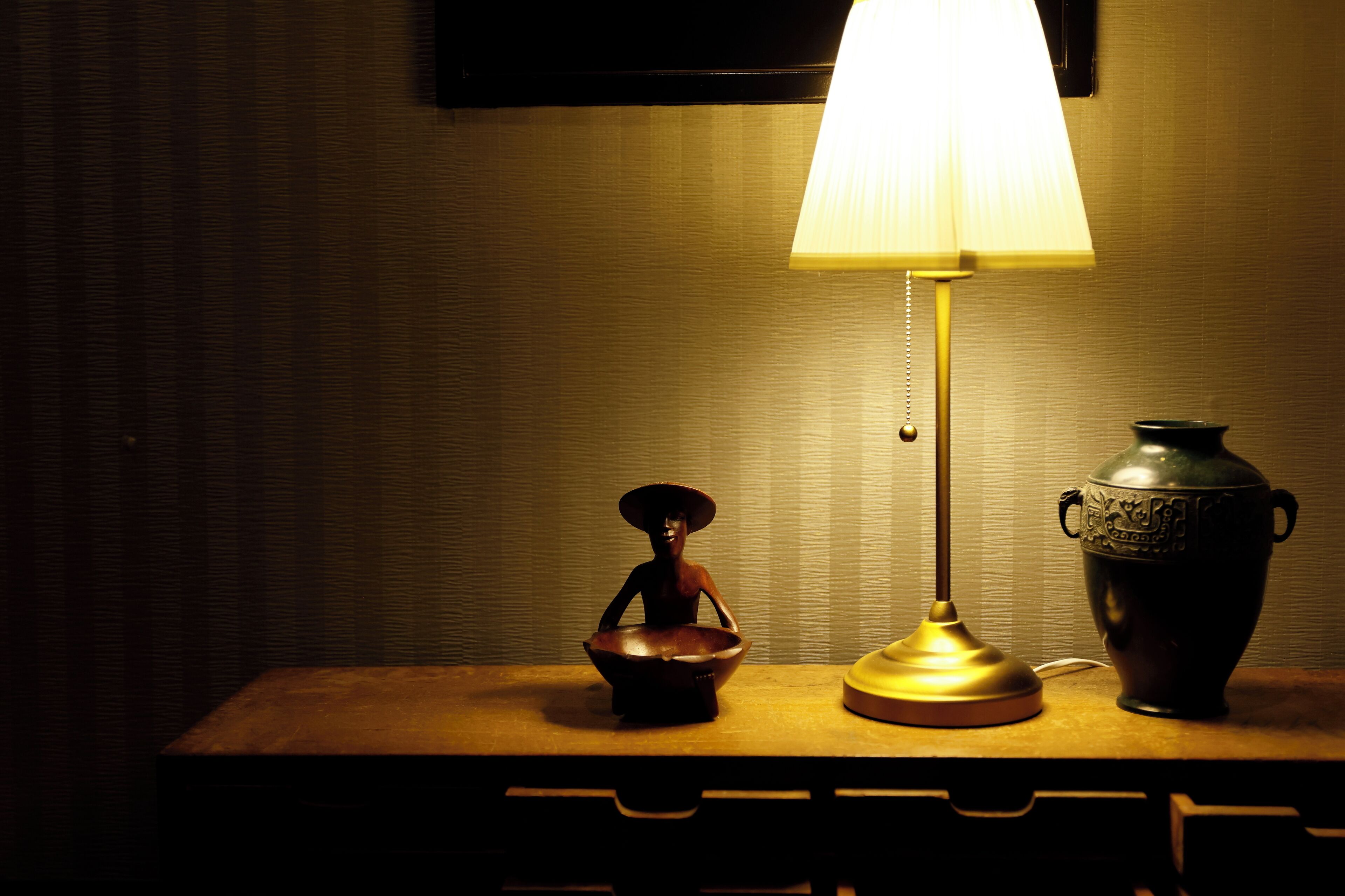 Uma mesa com uma luminária, uma tigela decorativa e um vaso.