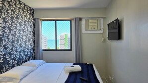 A hotel room with a bed, a window with a view, a wall-mounted air conditioner, and a TV. - Vista Mar na Pajuçara: Amplo 2Q p/ 6 Pessoas (Maceió)