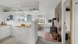 Une cuisine moderne avec des meubles blancs, un îlot central, un four encastré dans un mur de briques et une vue sur l’extérieur.
