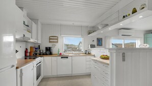 Une cuisine moderne avec des meubles blancs, un plan de travail en bois et une vue sur la plage.