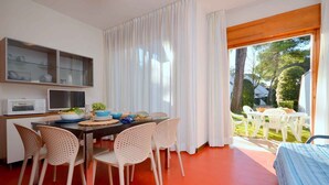 A modern kitchen with a dining area, a microwave, a TV, and a view of the garden. - Holiday apartment with terrace and air conditioning (Bibione)
