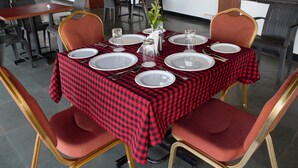 A dining area with a checkered tablecloth, red upholstered chairs, and a vase with a plant. - Palmarinha De Goa unit of GKP Real Estat (Calangute)