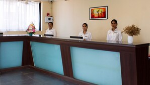 A reception desk with three staff members, a framed artwork on the wall, and a vase with dried flowers. - Palmarinha De Goa unit of GKP Real Estat (Calangute)