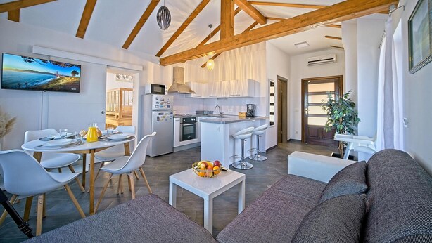 Une cuisine moderne avec des armoires blanches, un four encastré et un four à micro-ondes. On y trouve un coin repas avec une table et des chaises, ainsi qu’un salon avec un canapé et une table basse.