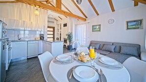 Une cuisine moderne avec des meubles blancs, un coin repas doté d’une table ronde préparée pour le petit-déjeuner, et un salon avec un canapé gris.