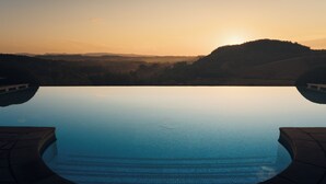 Une piscine aux eaux cristallines, avec une vue sur un coucher de soleil et des collines en arrière-plan.