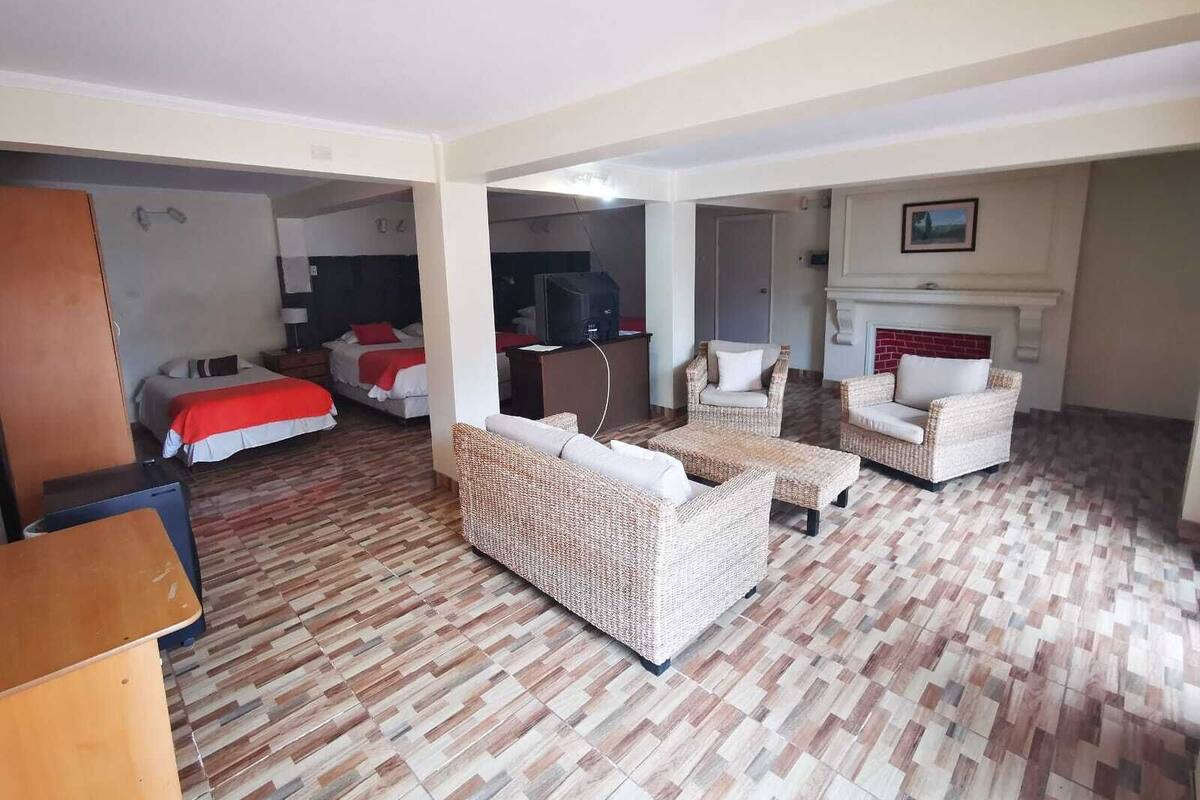 A hotel room with two beds, a desk, wicker furniture, a fireplace, and a television.