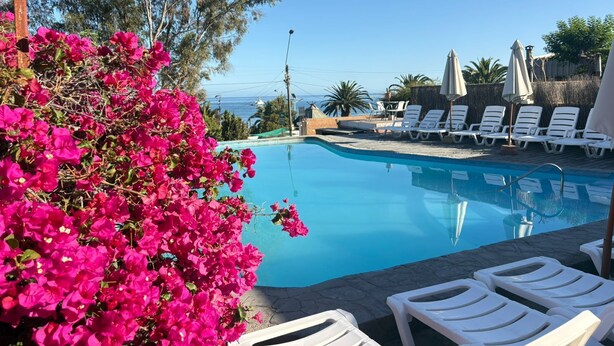 Zona de piscina con sillas de descanso blancas y vista al océano.