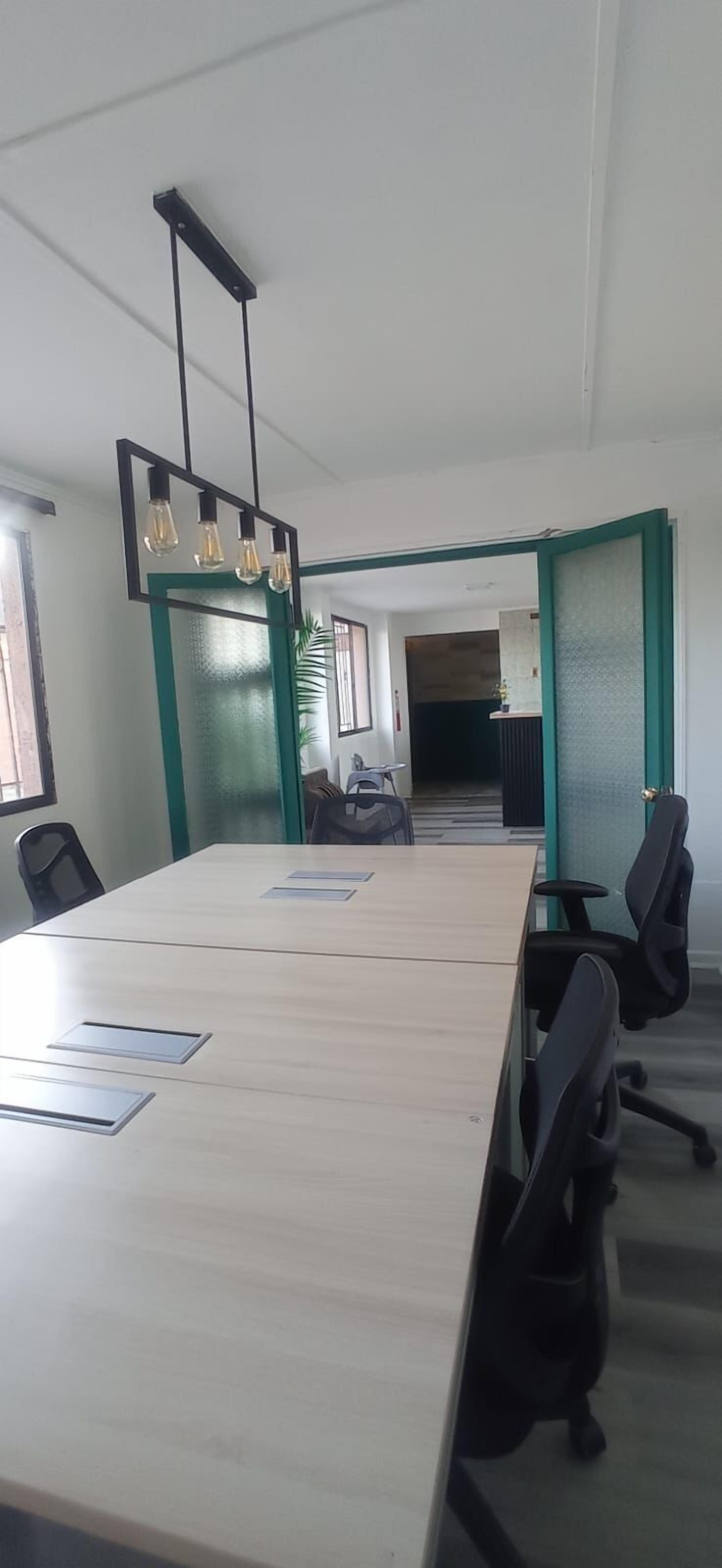 Un salón de conferencias con una larga mesa, sillas de oficina negras y una lámpara colgante.