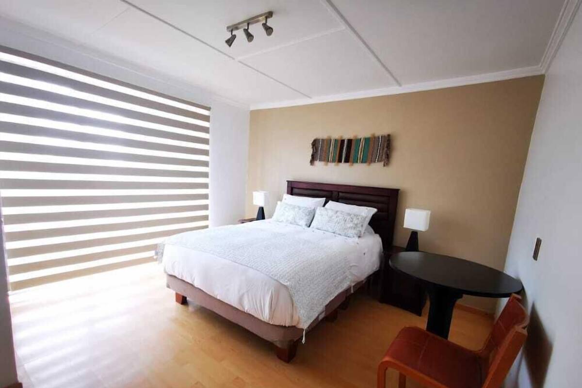 A hotel room with a large bed, a nightstand, a small table, and a chair.