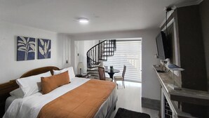 Habitación de hotel con cama, escritorio, silla, televisor y escalera que lleva a un balcón.