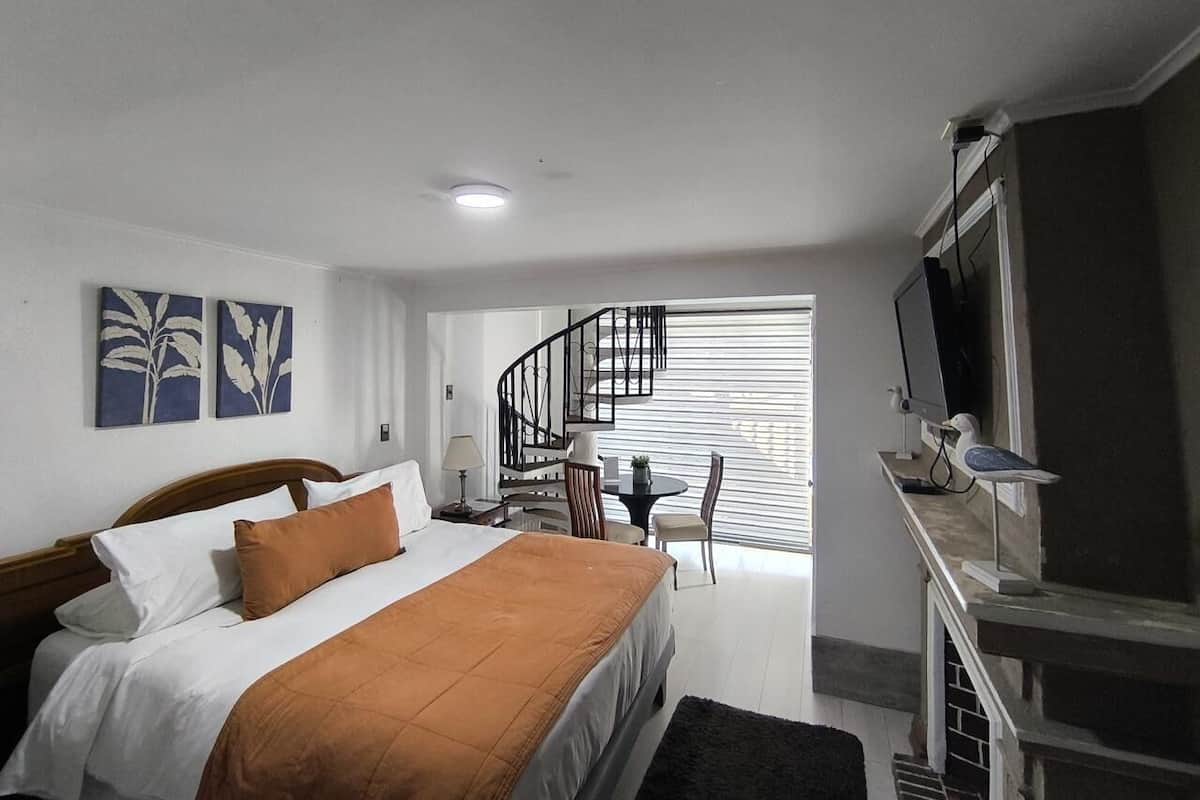 A hotel room with a bed, a desk, a chair, a TV, and a staircase leading to a balcony.
