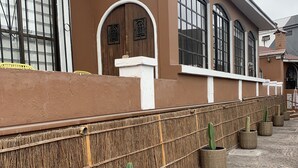 Un edificio con fachada marrón, ventanas amplias y una pared decorada con cestas tejidas que contienen cactus.