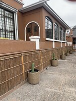 Un edificio con fachada marrón, ventanas amplias y una pared decorada con cestas tejidas que contienen cactus.
