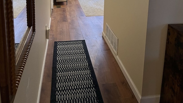 A hallway with a wooden floor, a black mat, a bench, and a bed with a patterned bedspread. - Historic Townsend Park bungalow minutes from Black Canyon National Park (Montrose)