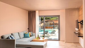 Un salon moderne avec un canapé gris, une table basse sur laquelle se trouvent des fruits et une bouteille, et une vue sur un espace extérieur avec une piscine.