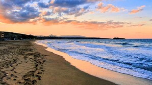 Une plage où l’on voit des empreintes de pas menant à l’eau, une montagne lointaine et un ciel au coucher du soleil.