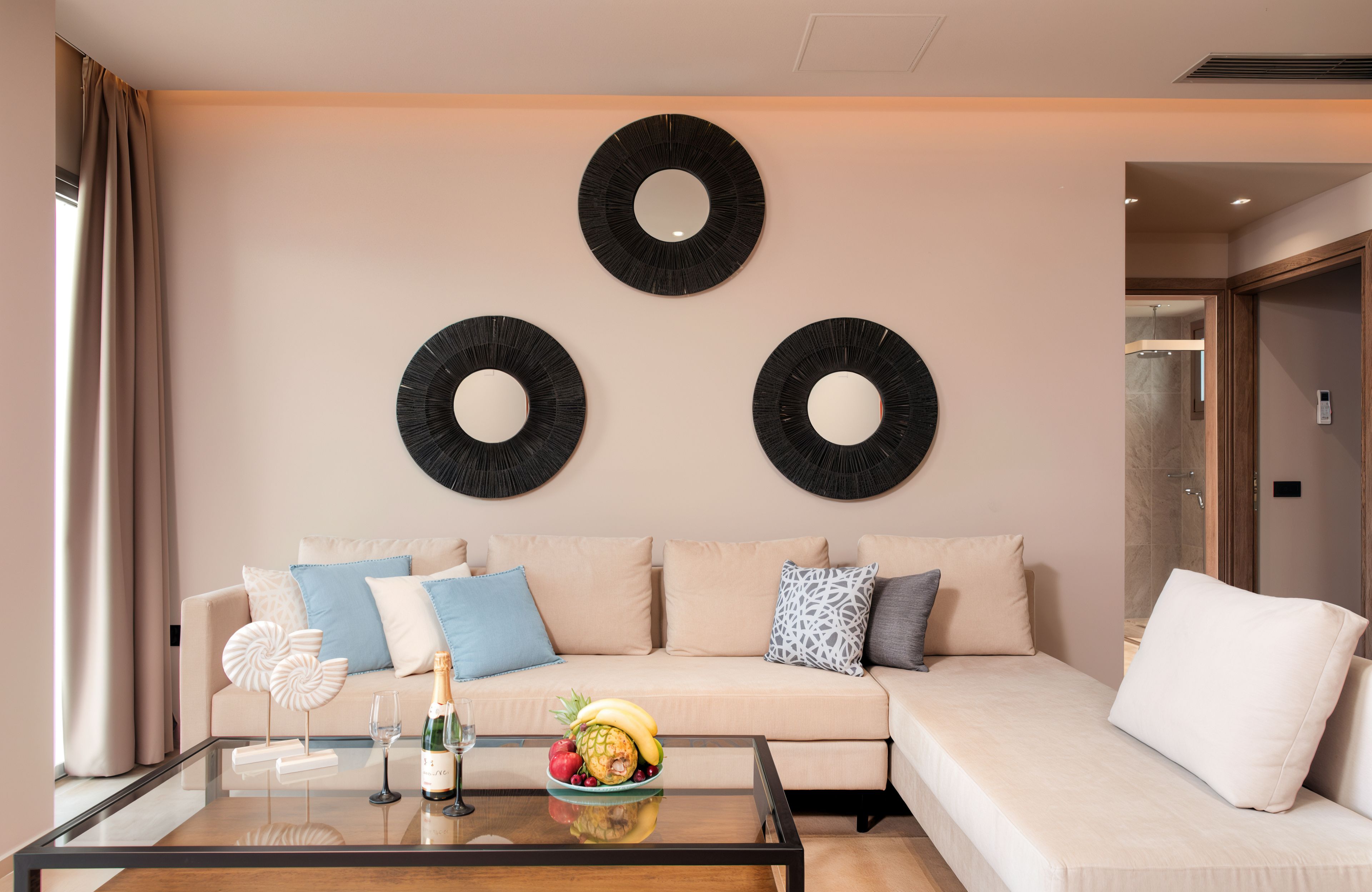 Ein modernes Wohnzimmer mit einem beigefarbenen Sofa, einem Glastisch und drei runden Wandspiegeln.