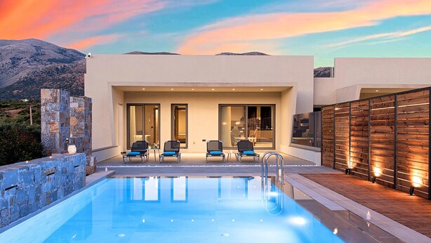 Un espace piscine extérieur moderne, offrant une vue dégagée sur les montagnes en arrière-plan, avec un mur en pierre d’un côté et une terrasse en bois de l’autre.