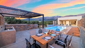 Un espace repas aménagé au bord de la piscine, avec une table pour deux, une pergola et une vue sur les montagnes.