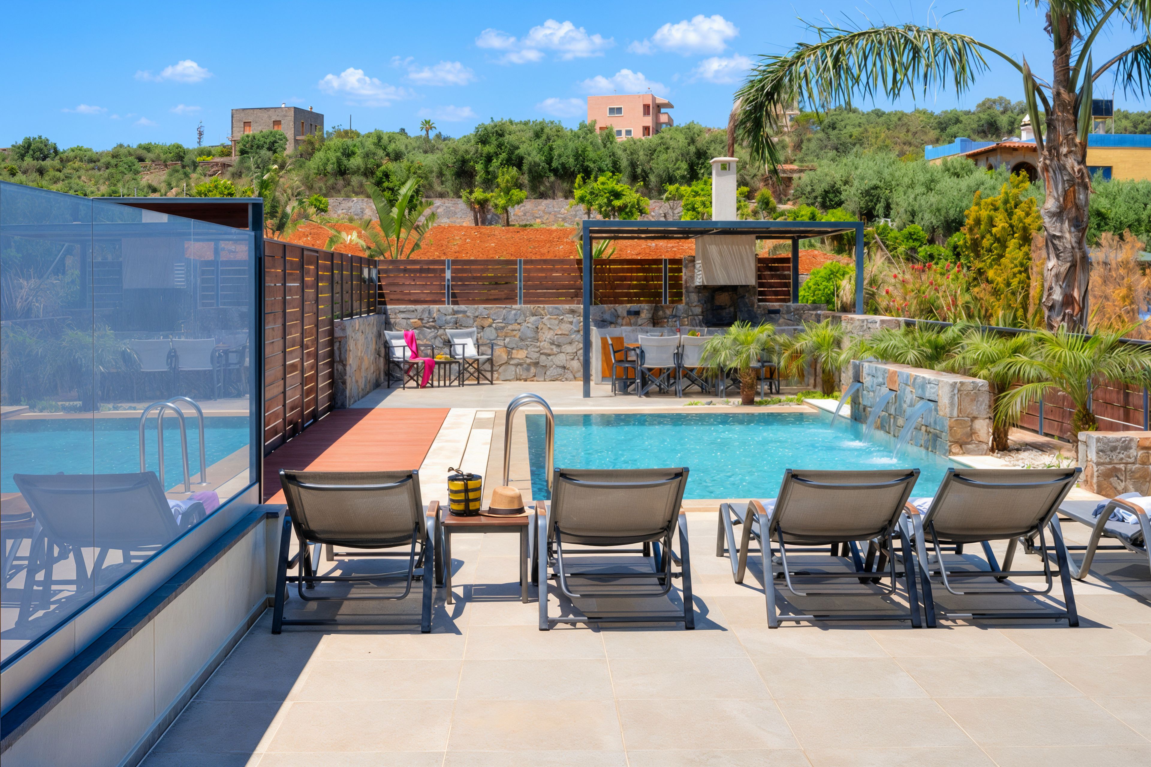 Área da piscina com espreguiçadeiras, mesa e parede de pedra.