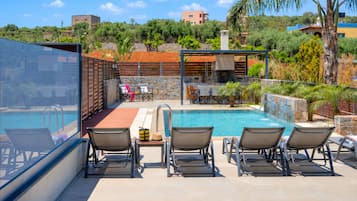Área da piscina com espreguiçadeiras, mesa e parede de pedra.