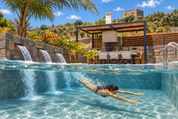 Una piscina con cascada, zona de estar cubierta y pared de piedra.