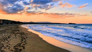 Une plage où l’on voit des empreintes de pas menant à l’eau, une montagne lointaine et un ciel au coucher du soleil.