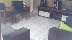 Een woonkamer met een televisie, een koffiezetapparaat en een open haard. Er staan twee stoelen en een bank.