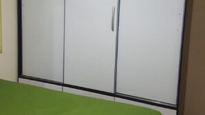 Een slaapkamer met een groen sprei, een witte garderobe met zwart frame en een betegelde vloer.