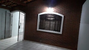 Een gang met een bakstenen muur, een raam met metalen tralies en een deur met een metalen hekwerk.