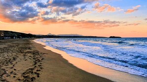 Une plage où l’on voit des empreintes de pas menant à l’eau, une montagne lointaine et un ciel nuageux.