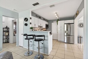 A modern kitchen with white cabinets, a stainless steel refrigerator, and a bar area with two stools.