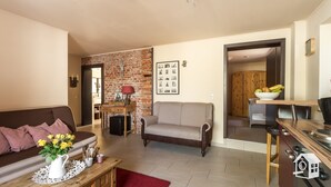 Un salon comprenant un canapé, une table basse ornée d’un vase de fleurs, un mur en briques et un coin repas avec une table et des chaises.