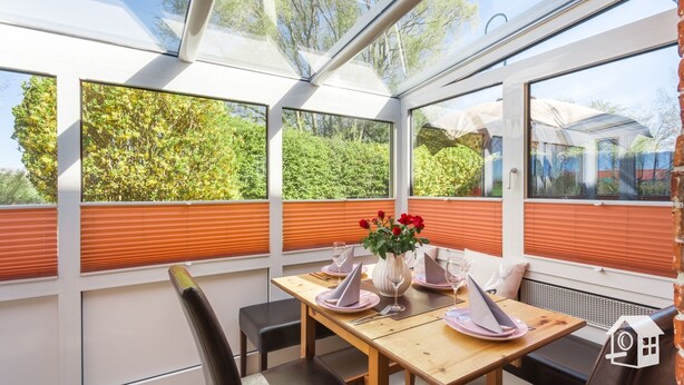 Une véranda avec une table à manger dressée pour deux personnes, agrémentée d’un vase de roses rouges et d’un verre de vin.