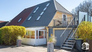 Un bâtiment à deux étages, doté d’un toit en pente, d’une entrée abritée et d’un escalier menant à un niveau supérieur.