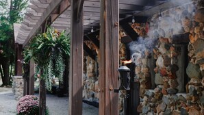 A stone building with a wooden porch, a hanging plant, and a lantern emitting smoke.